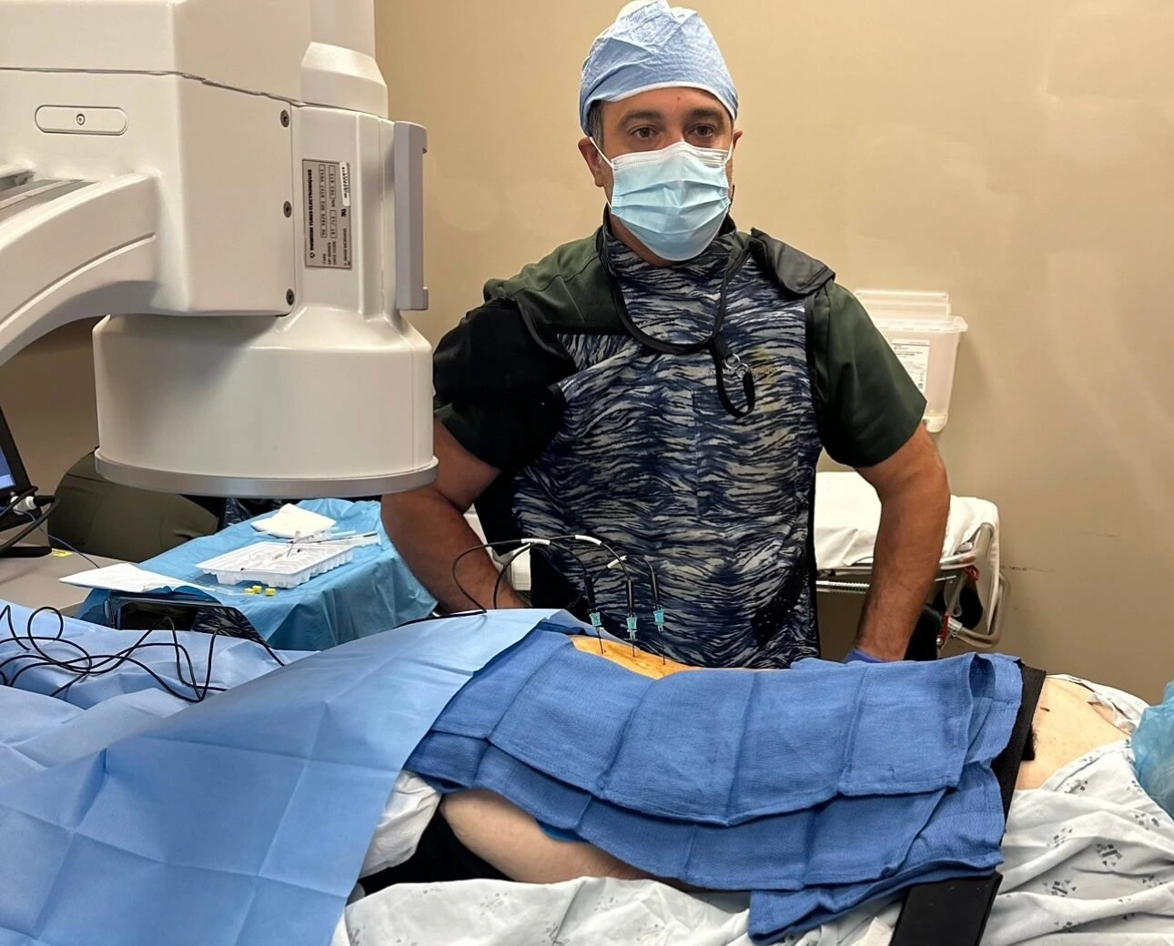 A man in a surgical mask standing next to a patient laying upside down, suffering from back pain.