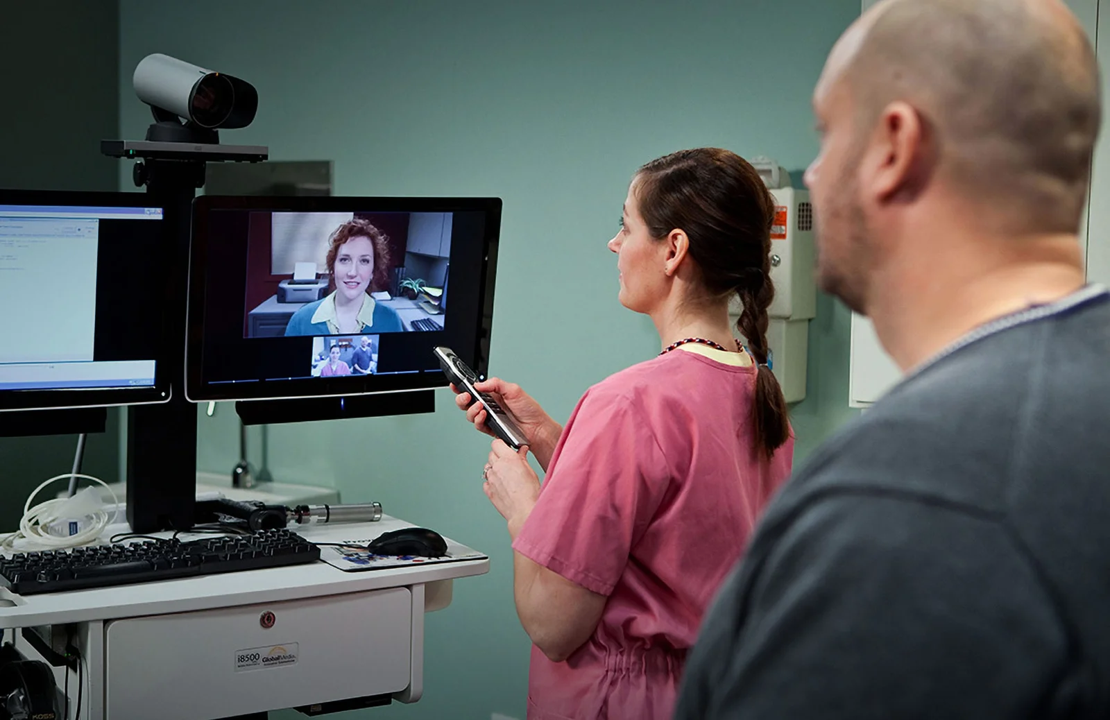 A female doctor facilitating an online consultation for a male patient with a specialist female doctor through a screen.